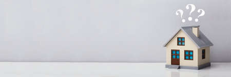 Small House Model With Question Marks Over Reflective Desk Against Grey Backgroundの写真素材