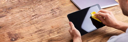 Man's Hand Cleaning Digital Tablet Screen With Soft Yellow Clothの写真素材