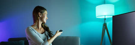 Happy Smiling Woman Controlling Electric Lamp With Mobile Phone At Home