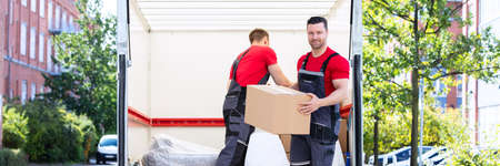 Two Young Men Unloading And Stacking The Brown Cardboard Boxes On Moving Truckの写真素材