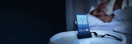 Man Waking Up With Alarm On Mobile Phone At Home