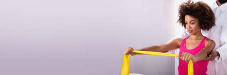 Physiotherapist Assisting Woman While Exercising With Exercise Bandの写真素材