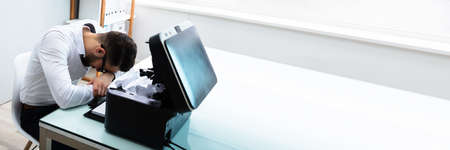 Tired Businessman Resting His Head In Front Of Paper Stuck In Printerの写真素材