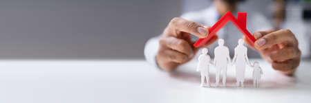 Close-up Of A Couple's Hand Protecting Family Figures With Red Roof