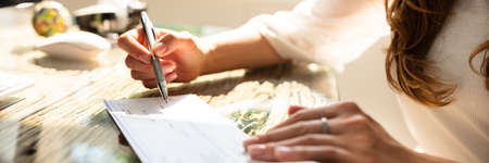 Businesswoman's Hand Signing Cheque On Wooden Desk