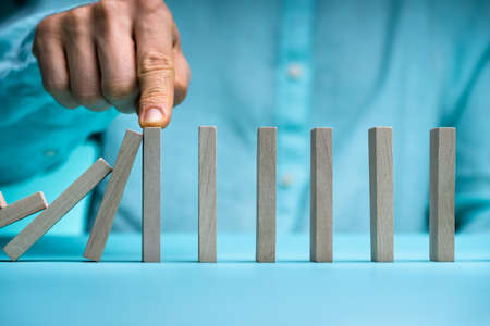 Close-up Of Businessman Stopping The Effect Of Domino With Hand At Deskの写真素材