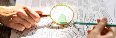 Close-up Of Human Hand Holding Magnifying Glass Over Paper Cadastre Map