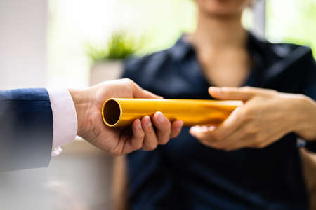 Close-up Of Businessman's Hand Passing The Golden Baton To His Partner In Officeの写真素材