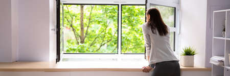 Side View Of A Woman Looking Through Window At Home