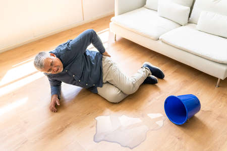 Mature Man Falling On Wet Floor In Front Spilled Bucket Of Water At Homeの写真素材