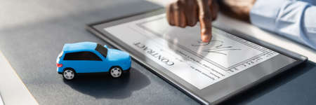 A Person's Hand Signing Car Loan Agreement Contract With Car Toy On Glass Deskの写真素材