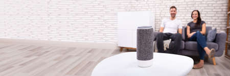 Couple Sitting On Sofa Listening To Music On Wireless Speaker