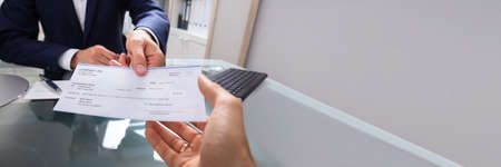 Businessman's Hand Giving Cheque Over Glass Desk