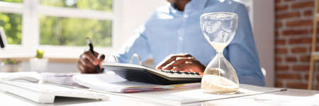 Hourglass In Front Of Businessperson Calculating Invoice