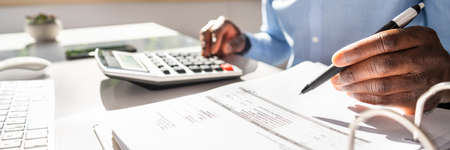 Happy Young Businessman Calculating Invoice On Computer Screen Near Laptopの写真素材