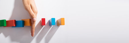 Close-up Of Businessperson Hand Stopping Colorful Blocks From Falling On Table In Officeの写真素材