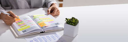 Close-up Of A Businesswoman Making Agenda On Personal Organizer At Workplace
