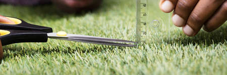 Close-up Of A Man Cutting Green Grass Measured With Ruler