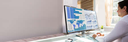 Young male stock market broker analyzing graph on computer at workplaceの写真素材