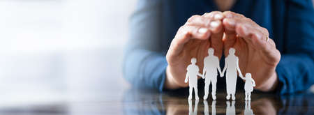 Close-up Of A Businessperson's Hand Protecting Family Figures On Wooden Deskの写真素材