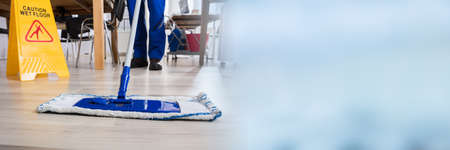 Janitor Cleaning Floor In Front Of Yellow Caution Wet Floor Sign