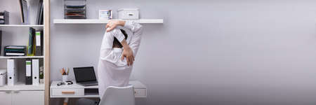 Rear View Of A Businessman Stretching His Arms In Office
