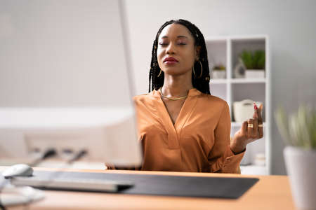 Full length of businesswoman mediating by computer on desk in officeの写真素材