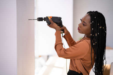 Portrait Of Young Woman Making Hole In Wall With Drill Machineの写真素材