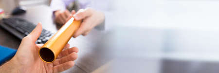 Close-up Of A Person's Hand Passing Golden Relay Baton To Businessmanの写真素材