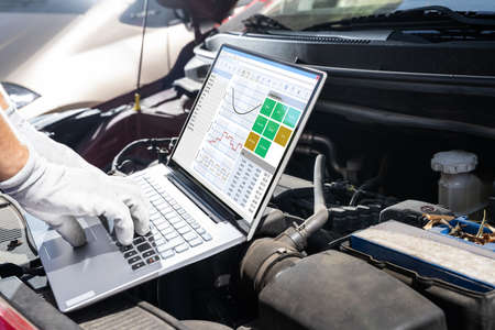 Young Male Mechanic Using Laptop While Examining Car Engineの写真素材
