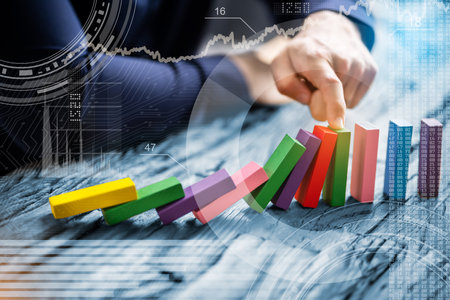 High Angle View Of A Businessperson Stopping Colorful Dominoes From Falling On Deskの写真素材