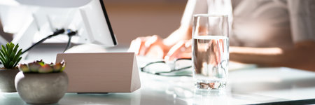 Water Glass On Desk And Woman In Foreground Using Computer