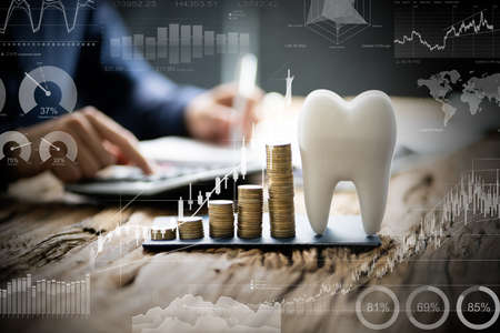 Close-up Of White Tooth Over Desk In Front Of Man Calculating Bill With Calculatorの写真素材