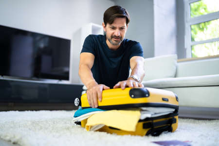 Man Packing Stuffed Suitcase Bag For Travelの写真素材