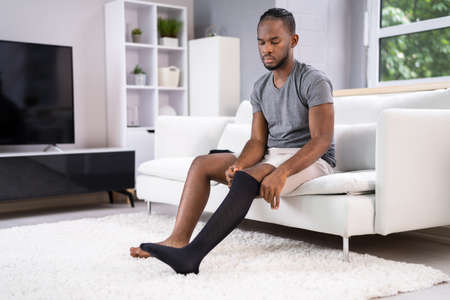 Man Putting On Medical Compression Stockings On Legsの写真素材