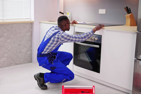 Young African Repairman Examining Stove In Kitchenの写真素材