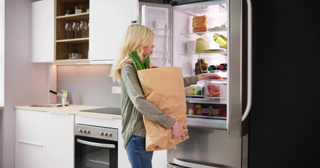 Woman With Grocery Bag Standing Near The Open Fridge With Healthy Food Productsの写真素材