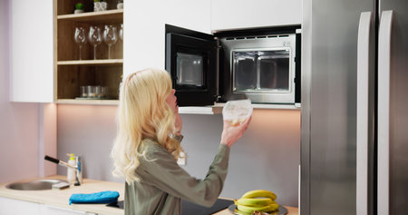 Woman Using Microwave Oven For Heating Food At Homeの写真素材