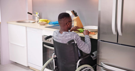 Young Disabled Man Sitting On Wheel Chair Preparing Food In Kitchenの写真素材