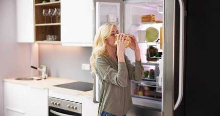 Young Woman Eating Sandwich In Front Of Refrigeratorの写真素材