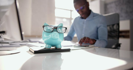 African Accounting Tax Advisor Using Calculator And Piggy Bankの写真素材