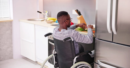 Young Disabled Man Sitting On Wheel Chair Preparing Food In Kitchenの写真素材