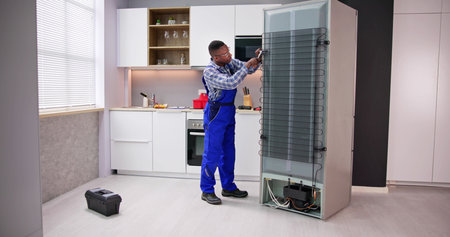 Young Male Serviceman Working On Fridge With Screwdriver At Homeの写真素材
