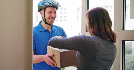 Happy Young Woman Accepting Parcel Box From Delivery Manの写真素材
