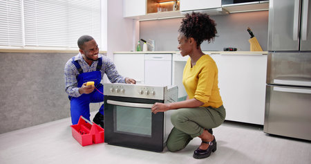 Smiling Repairman Repairing Oven On Kitchen Worktop In Front Of Womanの写真素材