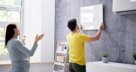 Beautiful Happy Woman Putting Picture Frame On Wall Of House