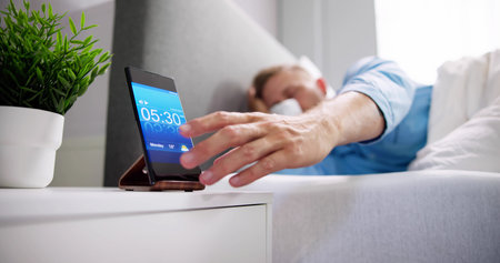Man Waking Up With Alarm On Mobile Phone At Home