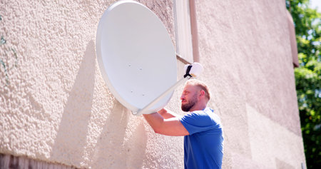 Young Male Technician In Uniform Installing TV Satellite Dish On Wallの写真素材