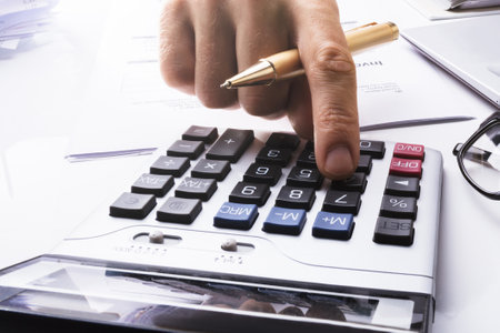 Midsection Of Businessman Calculating Tax Using Calculator With Laptop On Desk In Officeの写真素材