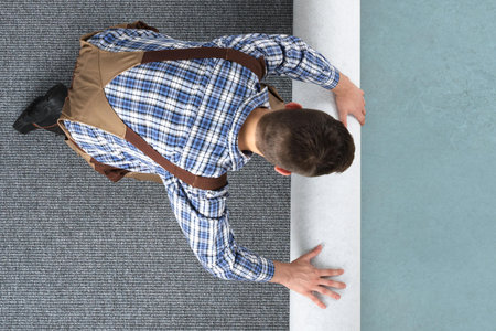 High Angle View Of Young Male Worker In Overalls Rolling Carpet On Floor At Homeの写真素材